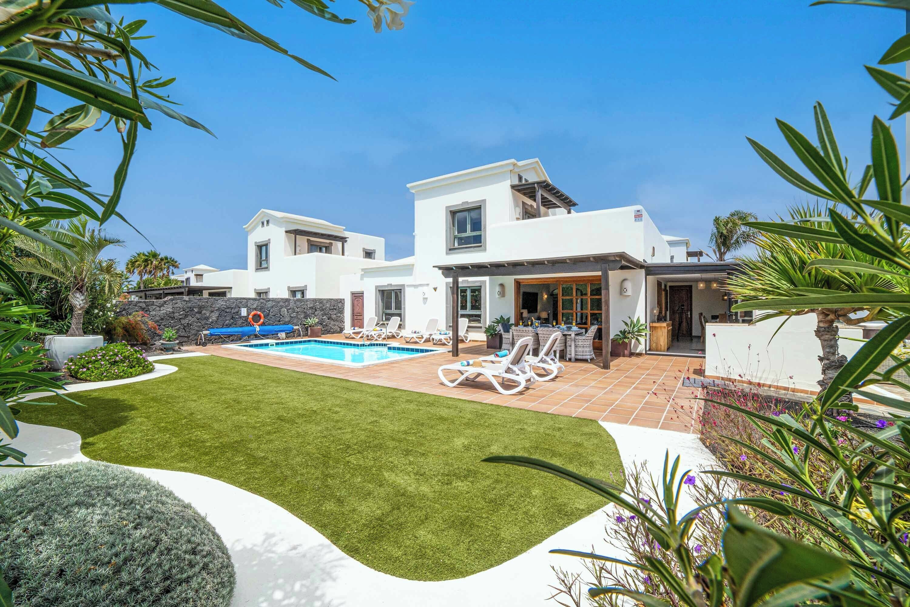 A modern two-story house with a swimming pool, outdoor seating, and a well-maintained lawn.