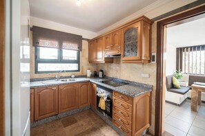 A kitchen with wooden cabinets, a built-in oven, and a window above the sink. - Villa Aguamarina - Three Bedroom Villa, Sleeps 6 (Playa Blanca)
