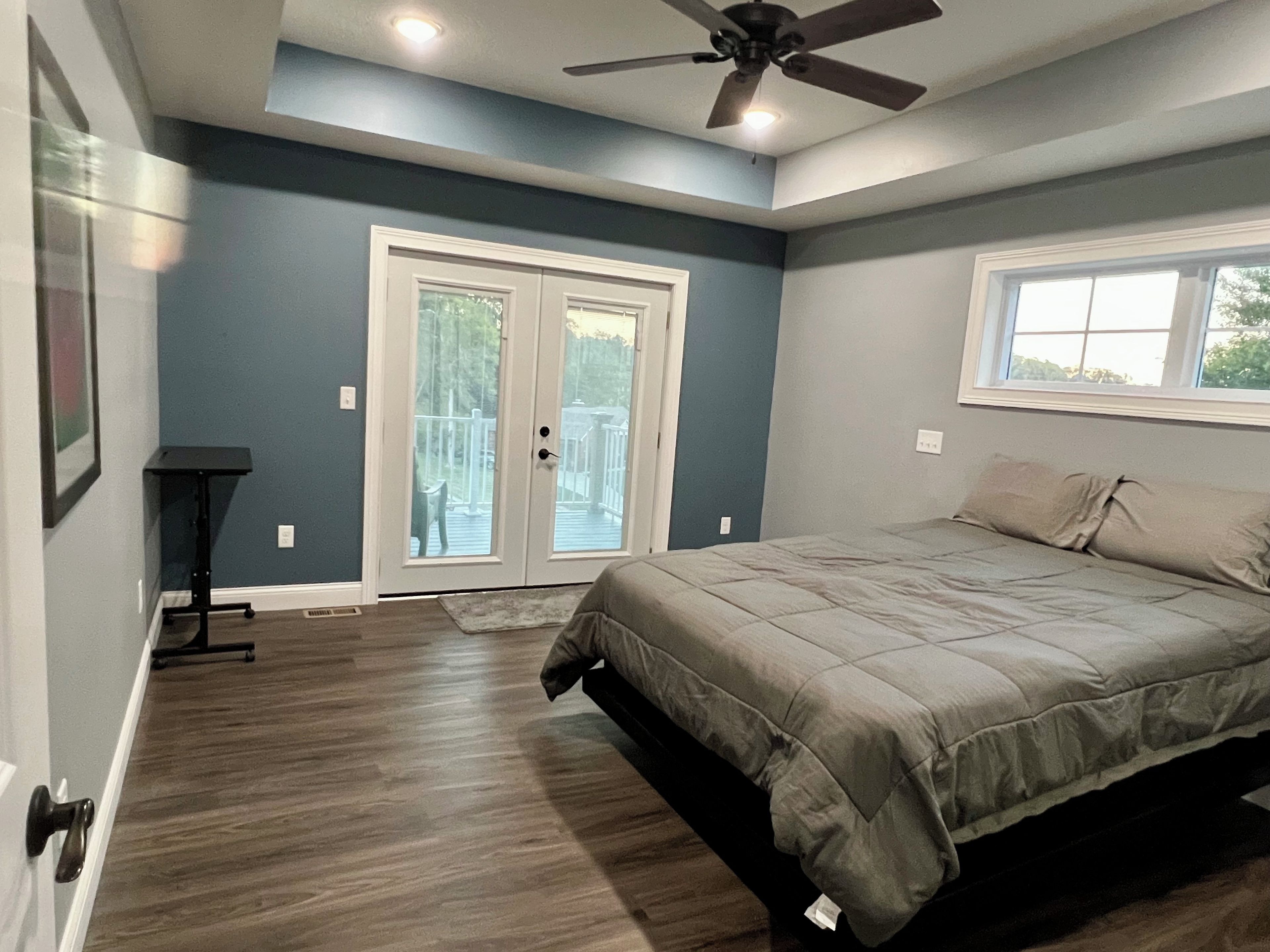 A bedroom with a bed, a ceiling fan, a window, and a door leading to a balcony.