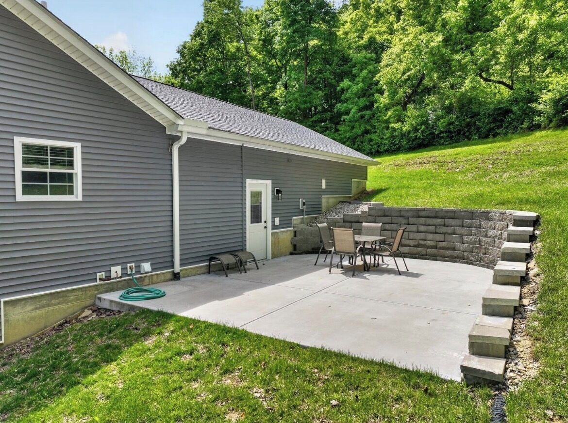 A residential property with a patio area, outdoor seating, and a stone retaining wall.