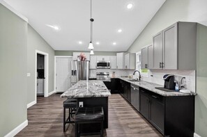 A modern kitchen with a marble island, stainless steel appliances, and a pendant light.