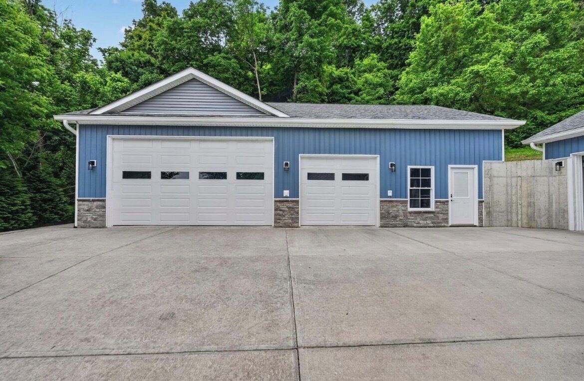 A two-story building with a garage, a small entry door, and a stone foundation.