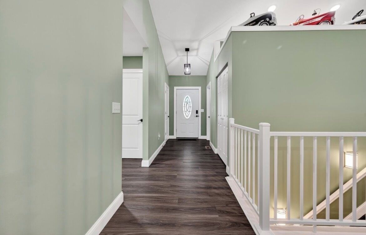 A hallway with a wooden floor, white railings, and a door with a decorative glass panel.