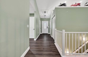 Un pasillo con piso de madera, barandillas blancas y una puerta con un panel de vidrio decorativo.
