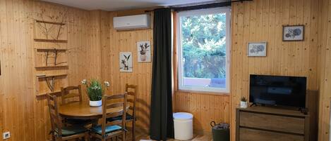 Una habitación con paneles de madera, una mesa de comedor, sillas, un sofá, un televisor y una ventana con vistas a árboles.