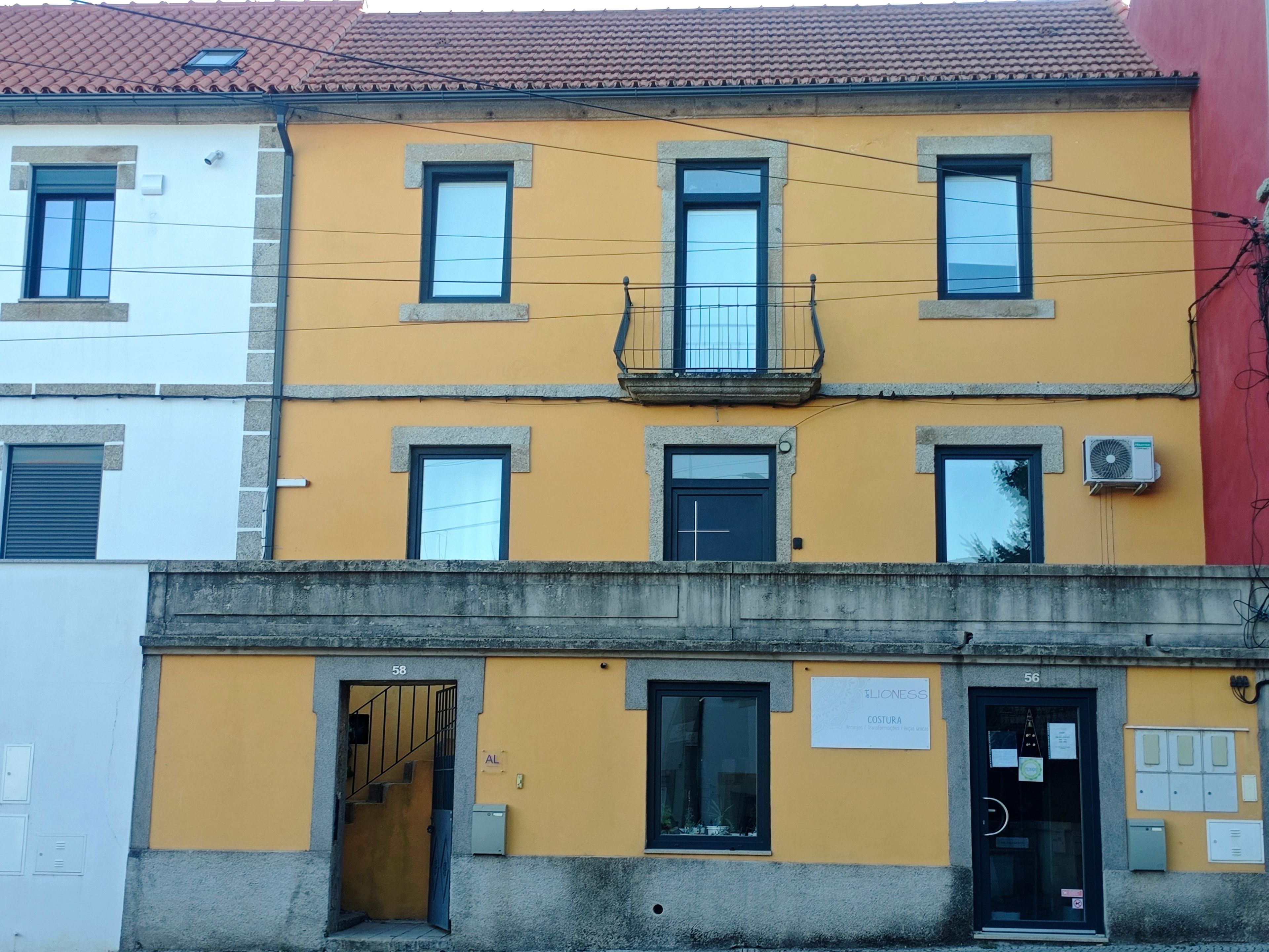 Edifício de vários andares com fachada amarela, várias janelas e entrada visível com porta identificada por 'AL'.