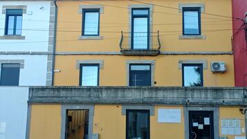 Edifício de vários andares com fachada amarela, várias janelas e entrada visível com porta identificada por 'AL'.