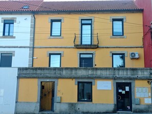 Un edificio de varios pisos con fachada amarilla, múltiples ventanas y una entrada visible con una puerta marcada 'AL'.