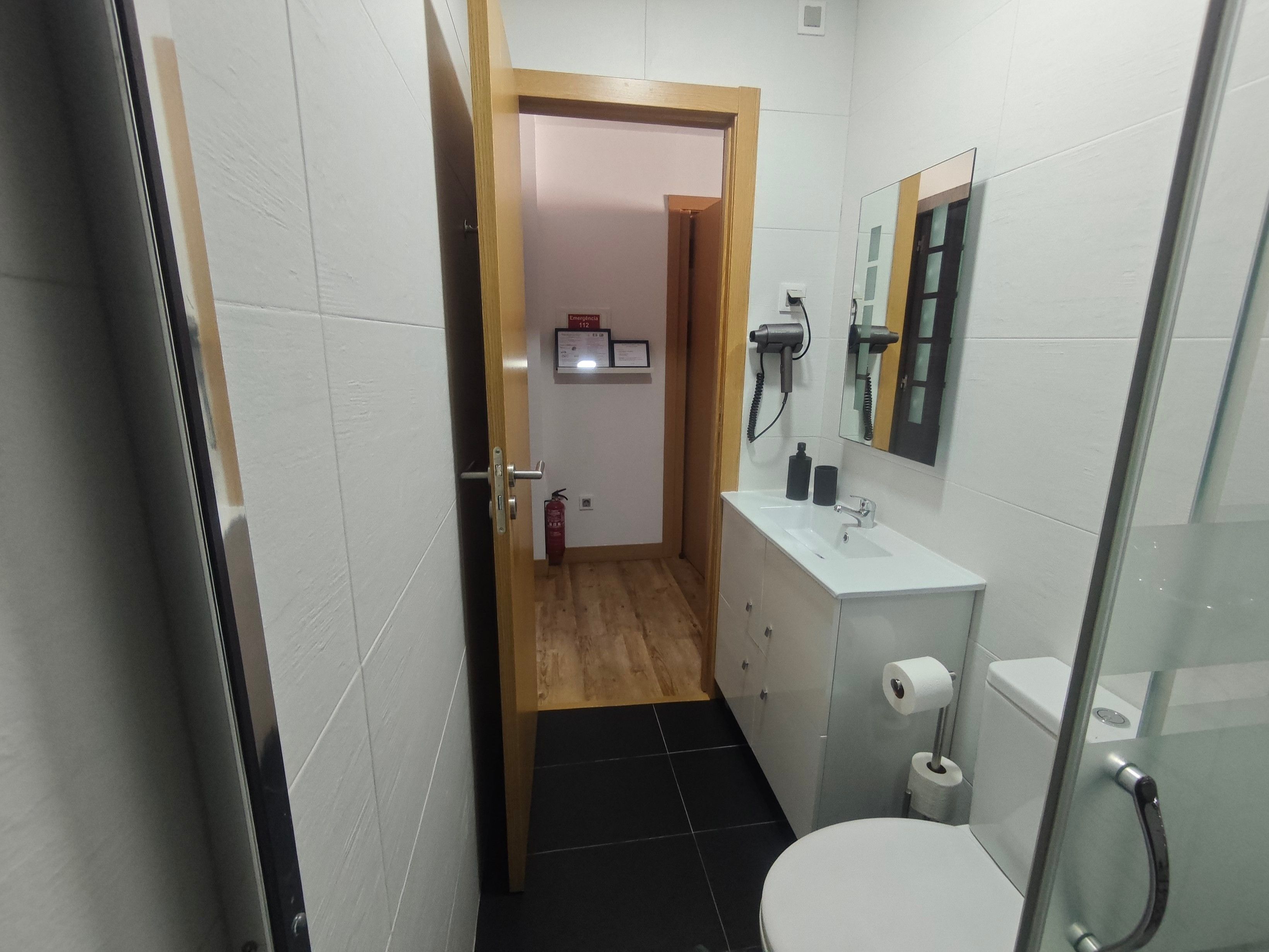 Un baño estrecho con un lavabo blanco, un inodoro y una zona de ducha.