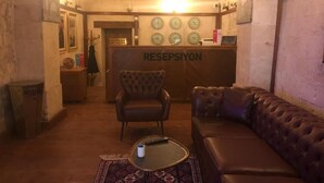 A lobby with a reception desk, a leather sofa, a small round table, and a patterned rug. - Ve Hotels (Sanliurfa)