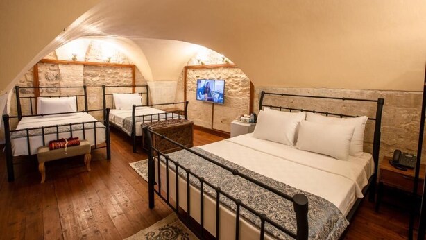 A cozy attic bedroom with three beds, a television, and a wooden floor. - Ve Hotels (Sanliurfa)