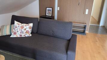 Una sala moderna con un sofá gris oscuro, un cojín estampado y una mesita con un posavasos tejido.