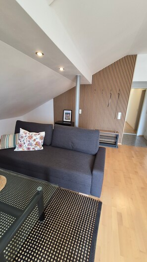 A modern living room with a dark grey sofa, a patterned throw pillow, and a small table with a woven placemat.