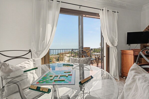 A room with a glass table, a board game, and a view of the sea through large windows.