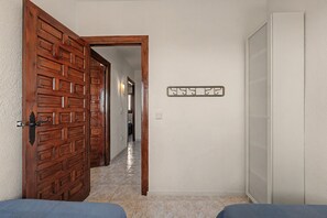 Un couloir avec une porte en bois sur la gauche, une porte blanche sur la droite et un luminaire fixé au mur.