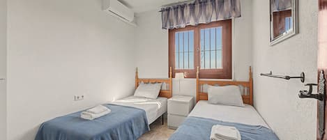Ein kleines, sauberes Zimmer mit zwei Einzelbetten, einem Fenster mit Vorhängen, einem Nachttisch und einer Klimaanlage.