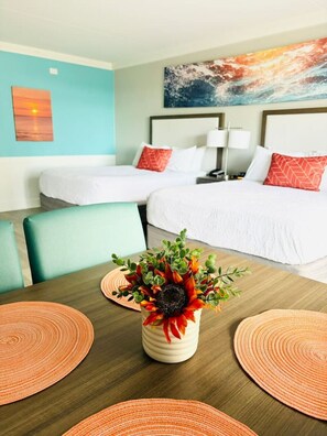 Ein Hotelzimmer mit zwei Betten, einem Esstisch mit Platzsets und einer Wand mit einem Gemälde.