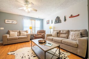 A living room with two sofas, a coffee table, a ceiling fan, and wall decorations. - Beary Cozy Condo, Hot Tub & Game Room, Dollywood (Sevierville)