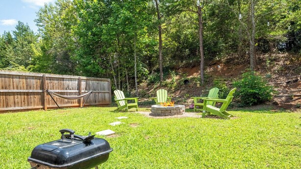 Ein Garten mit Grill, zwei Adirondack-Stühlen, einer Feuerstelle und einem Holzzaun.