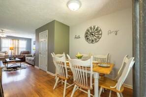 A dining area with a wooden table and white chairs, a wall clock, and a door leading to another room. - Beary Cozy Condo, Hot Tub & Game Room, Dollywood (Sevierville)