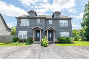 A two-story residential building with a symmetrical facade, a central entrance with a small porch, and a front yard with a well-maintained lawn and a single shrub. - Beary Cozy Condo, Hot Tub & Game Room, Dollywood (Sevierville)