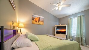 Ein Schlafzimmer mit einem Bett, einem Fernseher, einem Deckenventilator und einem Bild an der Wand.