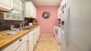Eine Küche mit weißen Schränken, einer Stein-Spritzschutzleiste, einer rosafarbenen Wand und einem Kühlschrank.