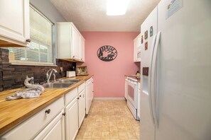 A kitchen with white cabinets, a stone backsplash, a pink wall, and a refrigerator. - Beary Cozy Condo, Hot Tub & Game Room, Dollywood (Sevierville)
