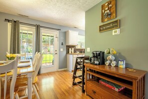Uma área de refeições com mesa posta para quatro pessoas, uma cozinha com armários brancos e um espaço para café com canecas.