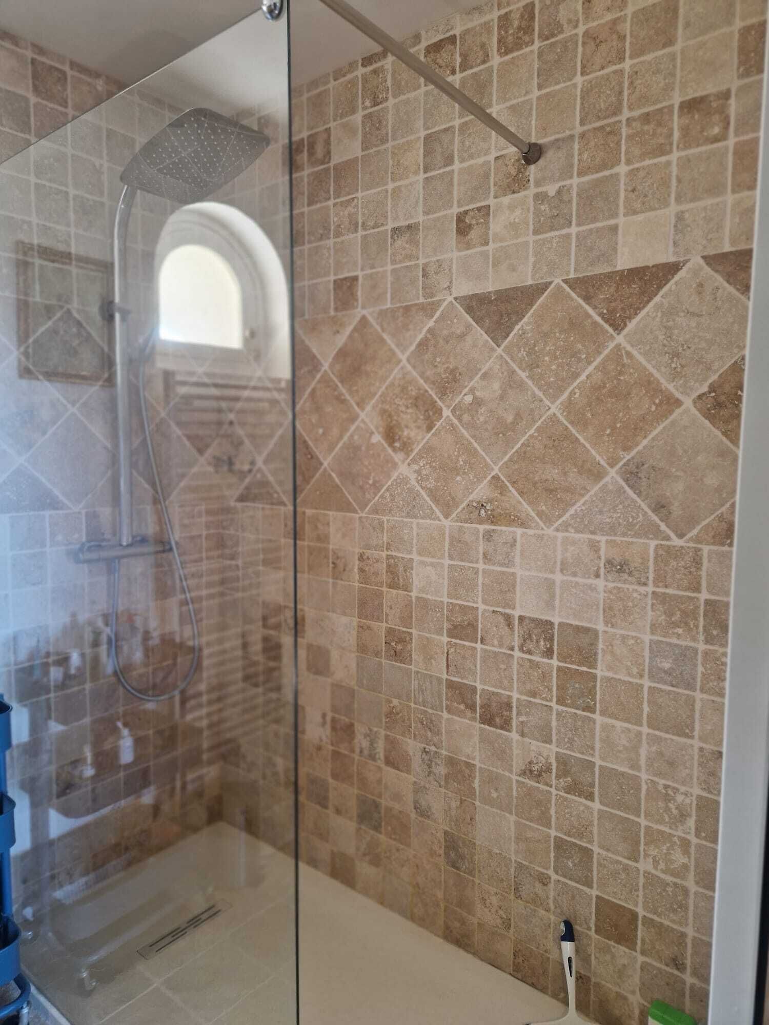 A shower area with a glass door, a showerhead, and a tiled wall.