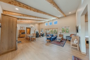 A spacious living area with a dining table, sofas, and a large window. - Peach Valley Vista - Sunset Views, Orchards & Wine Country Escape (Palisade)