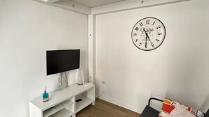 A modern living room with a flat-screen TV, a white entertainment unit, a black sofa with patterned cushions, and a large wall clock. - Bari Love Loft - Historic Center, Beach, Train Station, and Airport Just a Short Walk Away (Bari)