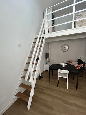 Eine Treppe führt zu einem Erkerbereich mit einem Esstisch und Stühlen, einer Uhr an der Wand und einem kleinen Beistelltisch mit einer Vase.