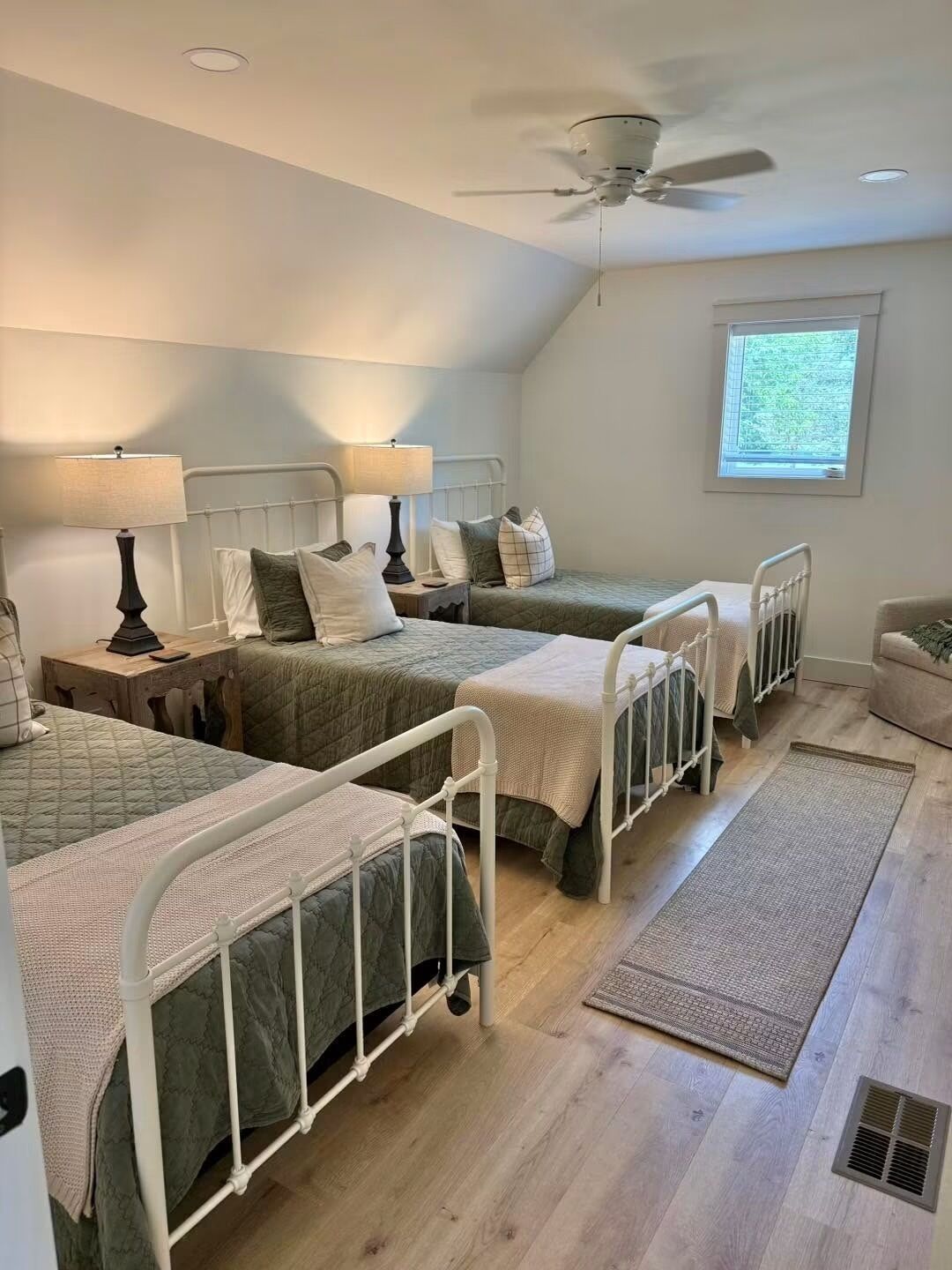 Une chambre avec deux lits, un ventilateur de plafond, une fenêtre et un radiateur.