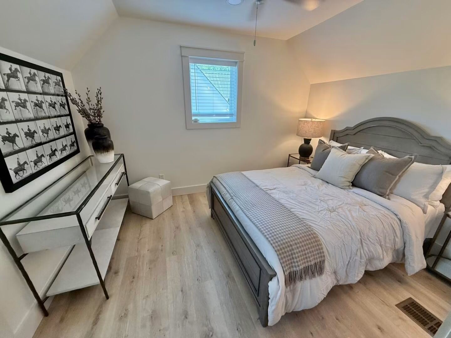 A bedroom with a bed, bedside tables, a nightstand, a window with blinds, and a wall-mounted artwork.