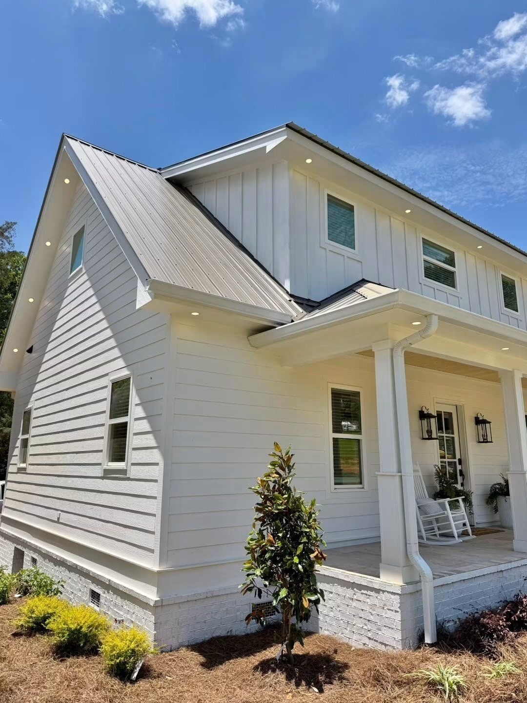 A two-story house with a front porch, a small tree, and a brick foundation.