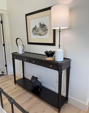 A dark wood console table with a white lamp, a framed picture, and a decorative bowl.