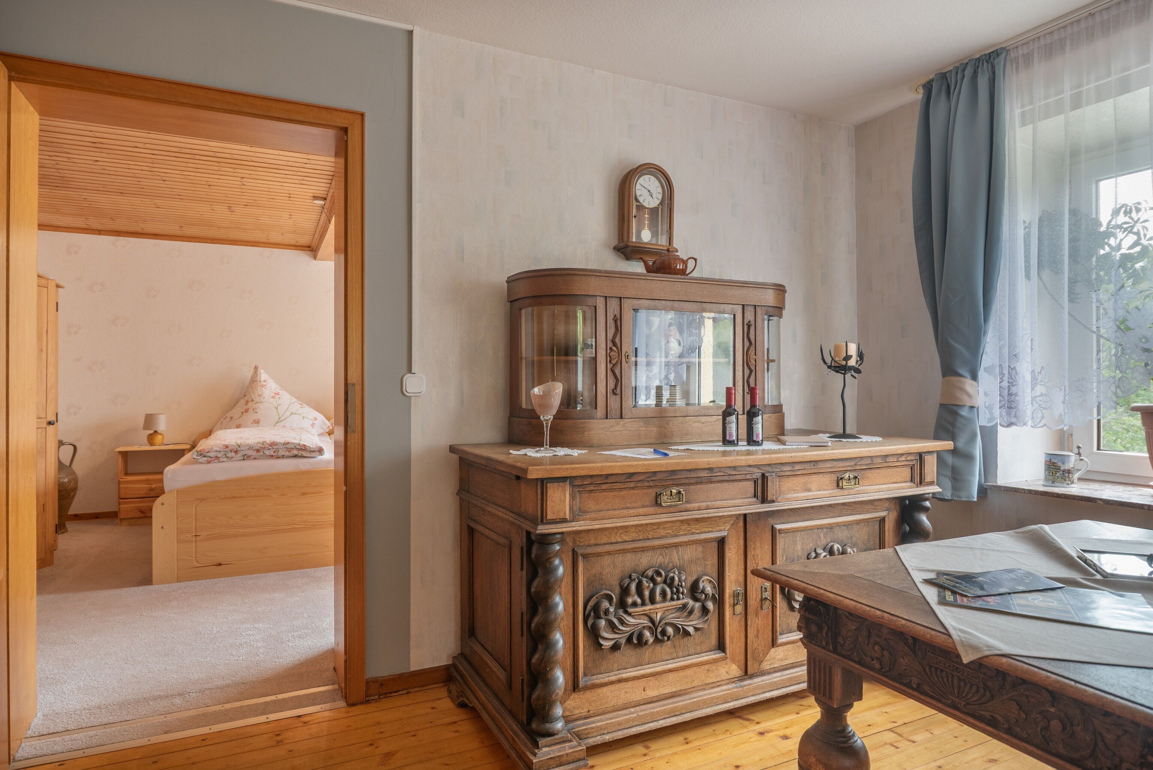 Ein Zimmer mit einem hölzernen Bett, einem Nachttisch aus Holz mit Spiegel und einem Fenster mit Vorhängen.