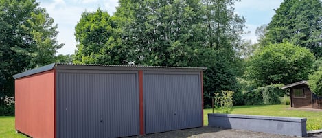 A two-car garage with a red accent wall, set in a grassy area with trees in the background.