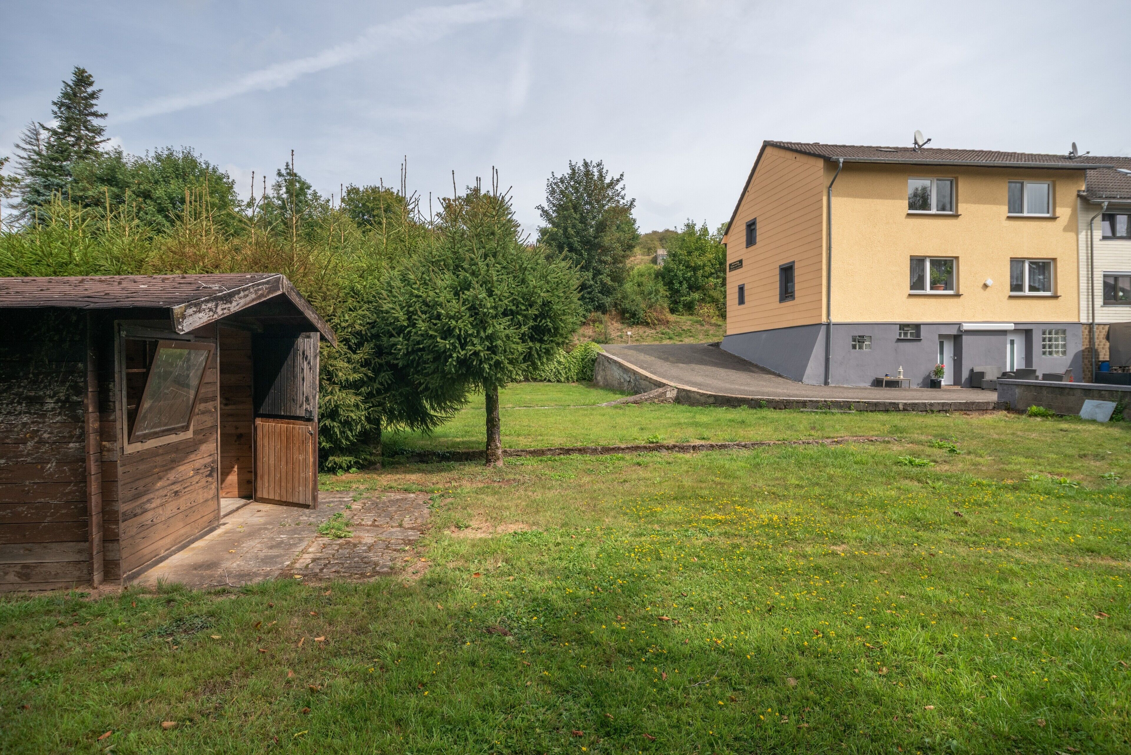 A residential area with a small wooden structure, a grassy yard, and a multi-story building with a yellow facade.