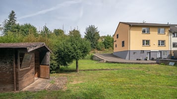 A residential area with a small wooden structure, a grassy yard, and a multi-story building with a yellow facade.
