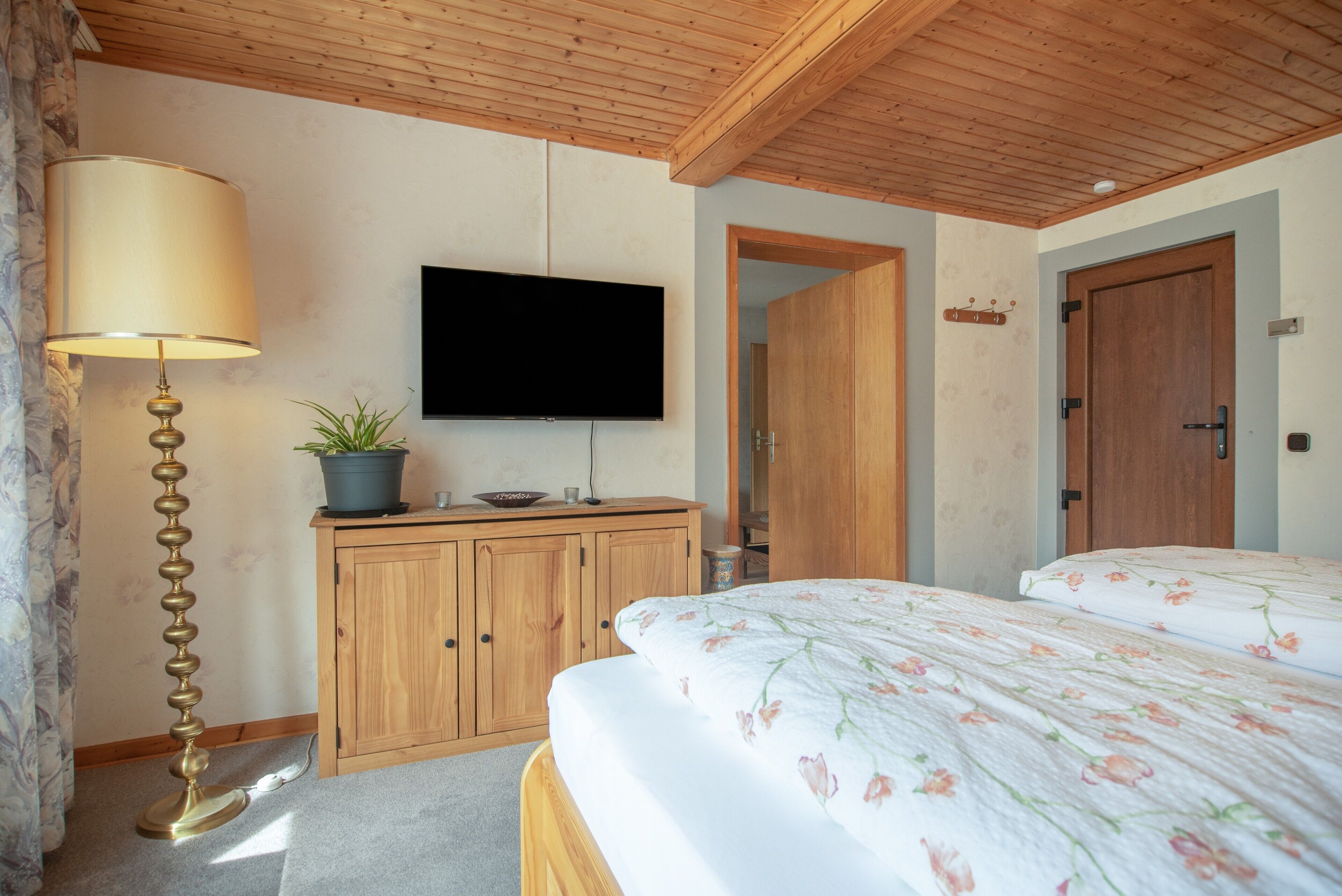 Ein Schlafzimmer mit einem Bett, einem an der Wand montierten Fernseher, einer hölzernen Kommode und einer Lampe.
