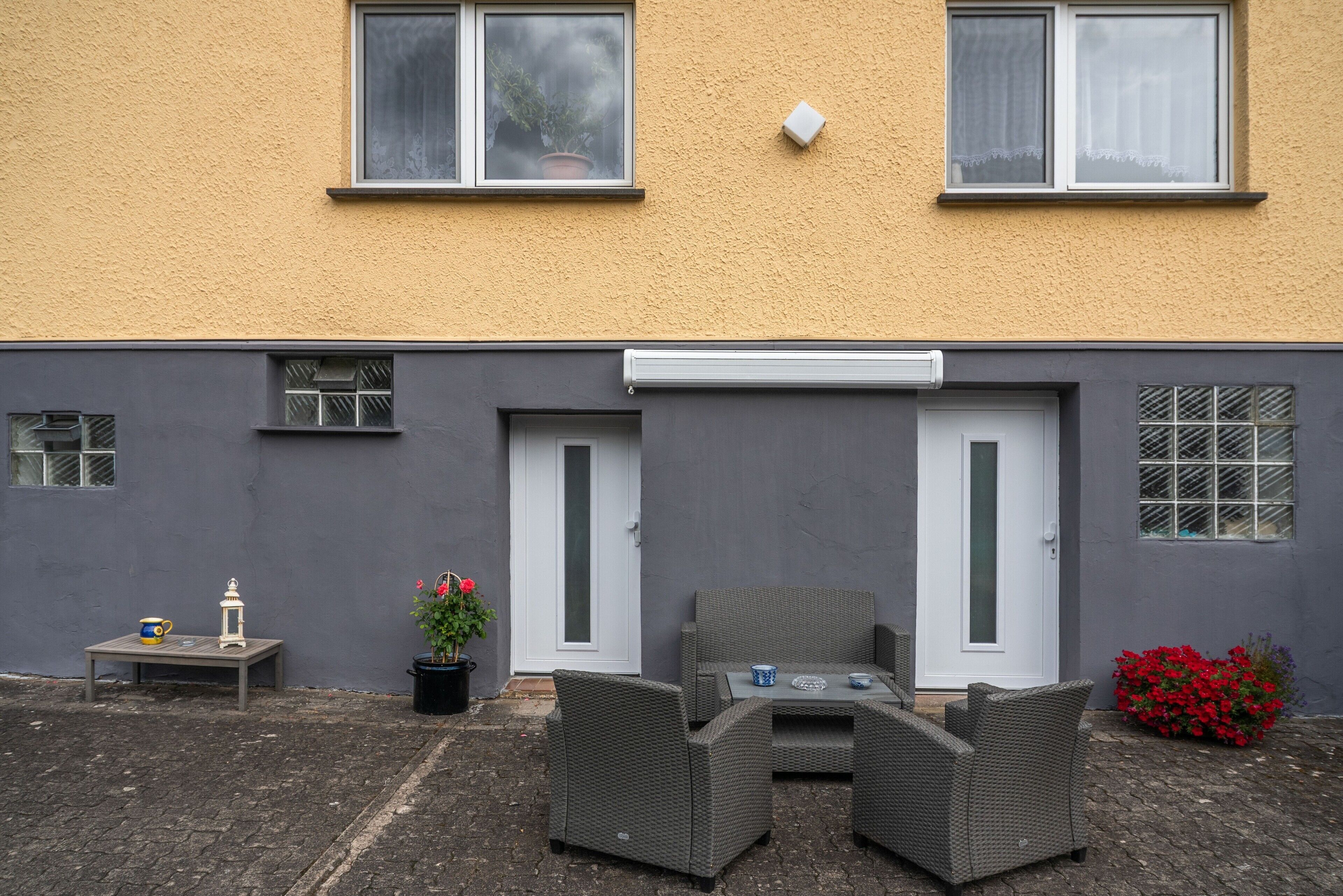 A residential building with a grey exterior, a white door, and a small patio area with wicker furniture and potted plants.