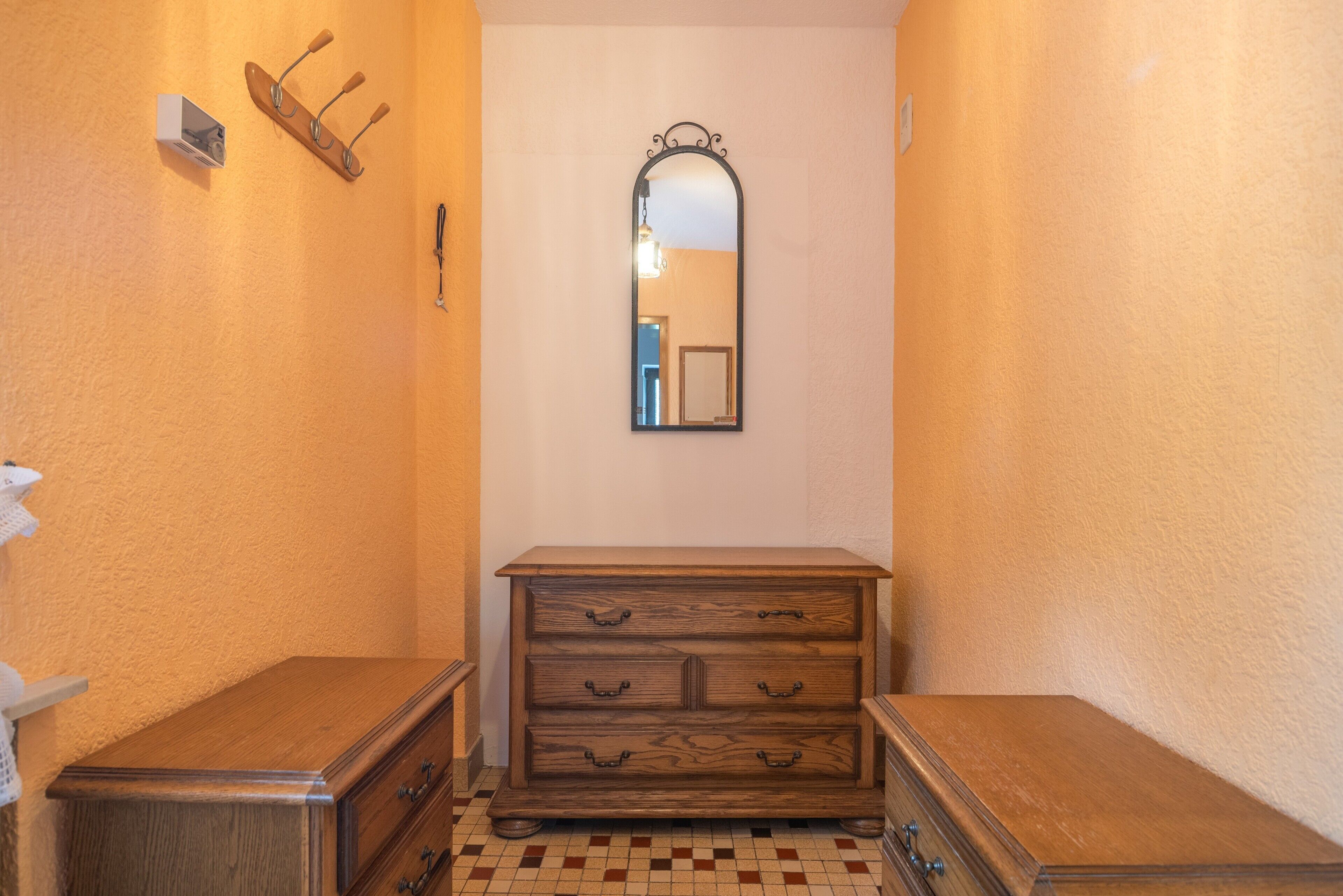A narrow hallway with a wooden dresser and a mirror on the wall.