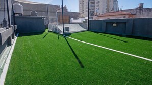Una azotea con césped artificial, una estructura de metal tipo jaula y edificios circundantes.