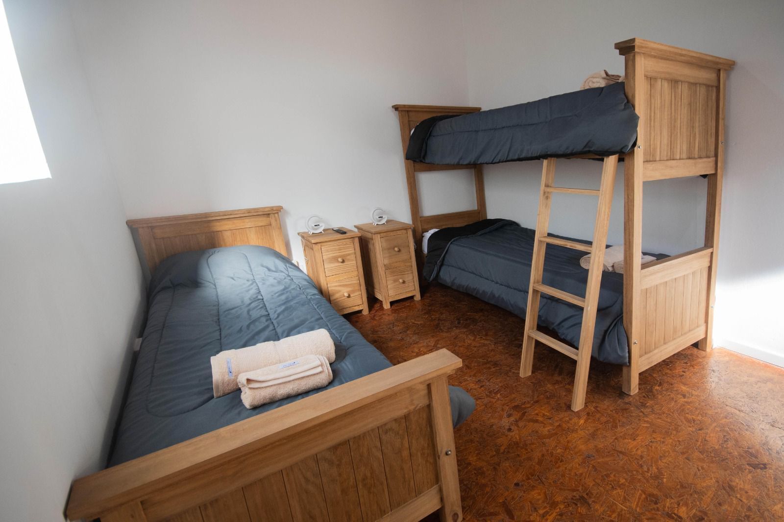 Una habitación con literas, una cama individual, muebles de madera y una mesita de noche pequeña.