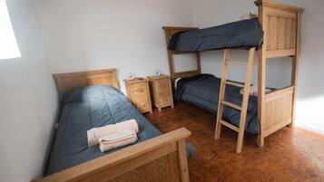 Una habitación con literas, una cama individual, muebles de madera y una mesita de noche pequeña.