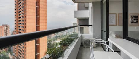 A balcony with a view of a tall building, a white table, and a chair.