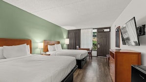 A hotel room with two beds, a desk, a chair, a television, and a door leading outside.