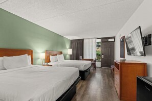 A hotel room with two beds, a desk, a chair, a television, and a door leading outside.
